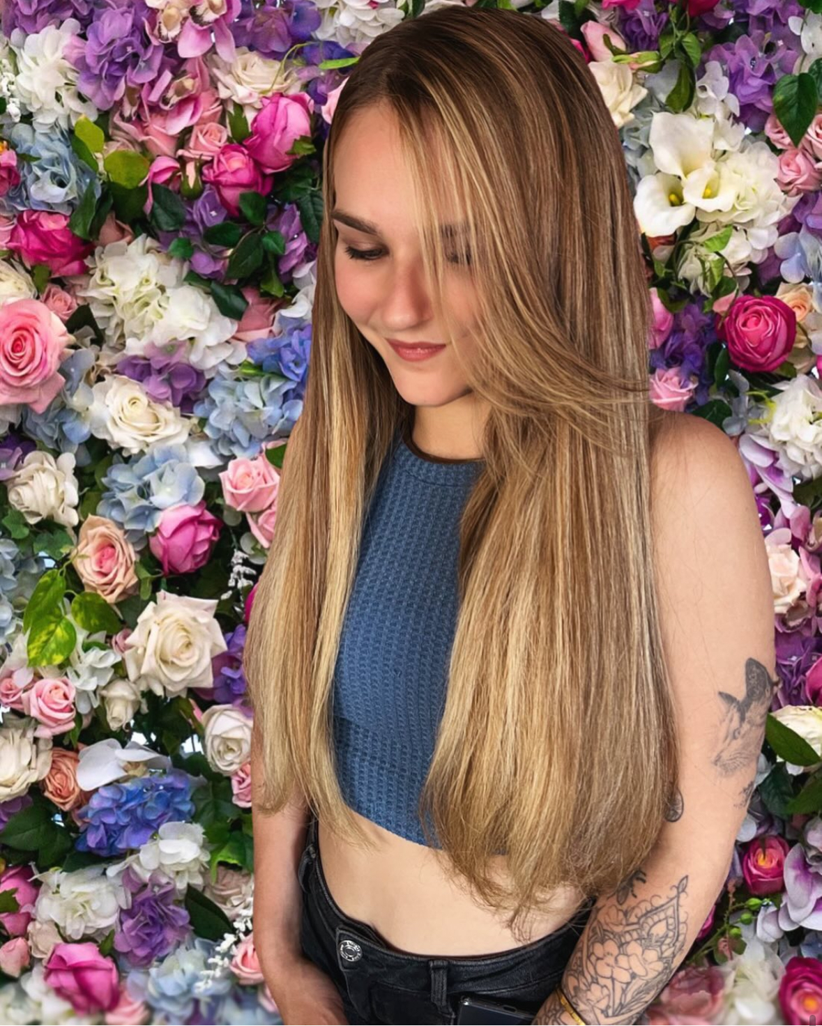 Een professionele haarstylist van Annas Hairextensions is bezig met het aanbrengen van haarextensies bij een tevreden klant. De stylist werkt zorgvuldig en met aandacht voor detail, terwijl de klant in de spiegel kijkt en glimlacht. De setting is een moderne kapsalon met een warme en uitnodigende sfeer.