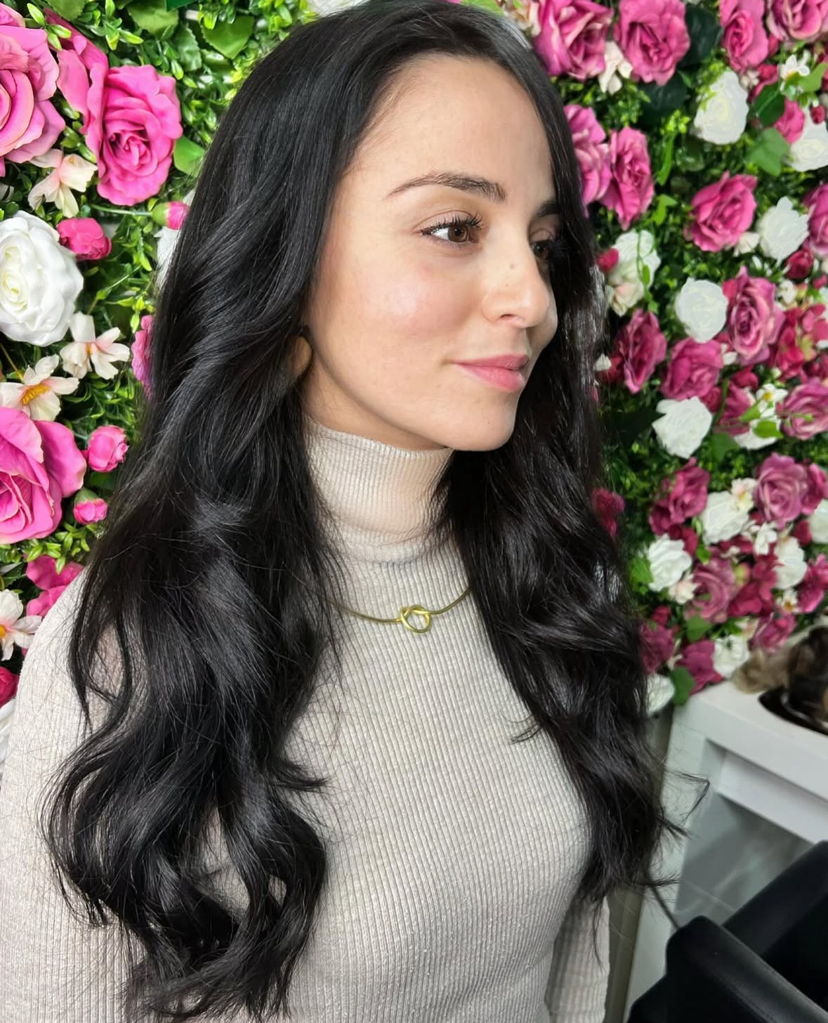 Een vrouw met een stralende glimlach zit in een moderne kapsalon terwijl een professionele stylist haar haar verlengt met hoogwaardige haarextensions. De stylist werkt zorgvuldig en gebruikt een combinatie van technieken om een natuurlijke en volumineuze look te creëren. Op de achtergrond zijn verschillende haarkleurstalen zichtbaar, wat de diversiteit aan mogelijkheden benadrukt voor het personaliseren van de extensions.